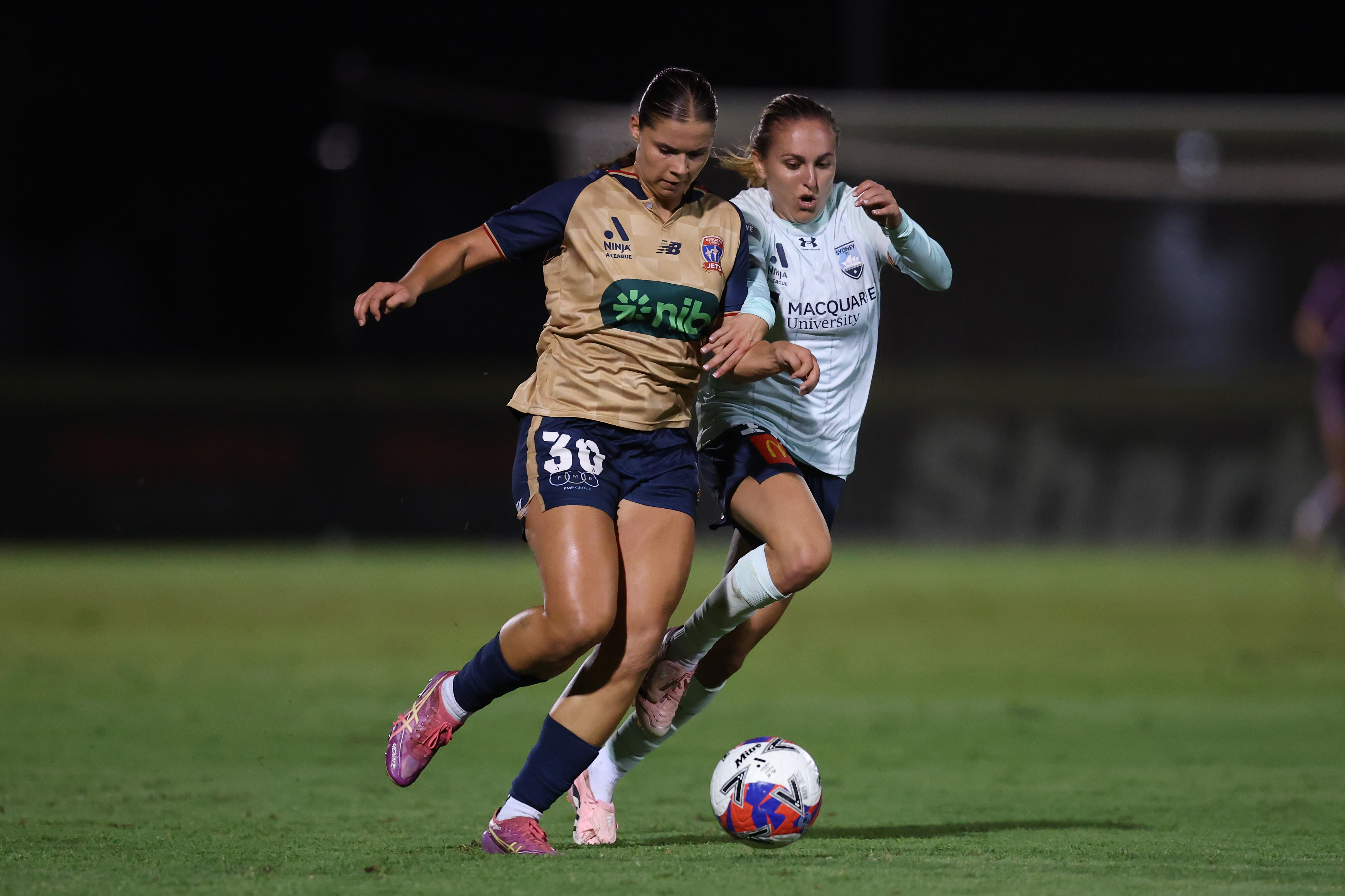 Newcastle Jets striker Alexis Collins in the club's gold away kit, wearing number 30, shielding the ball from a Sydney FC opponent during a night match
